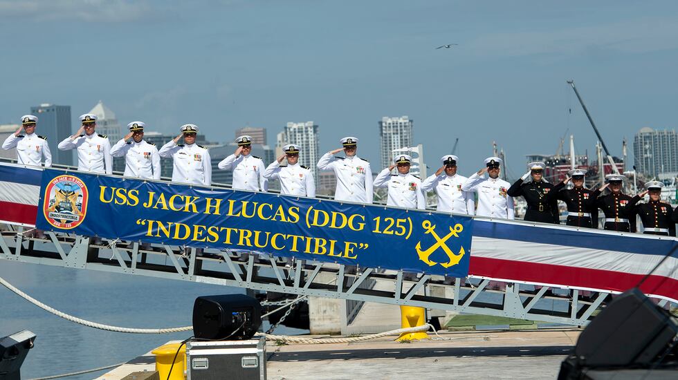 Sailors and U.S. Marines salute during the commissioning ceremony for the Arleigh Burke class...