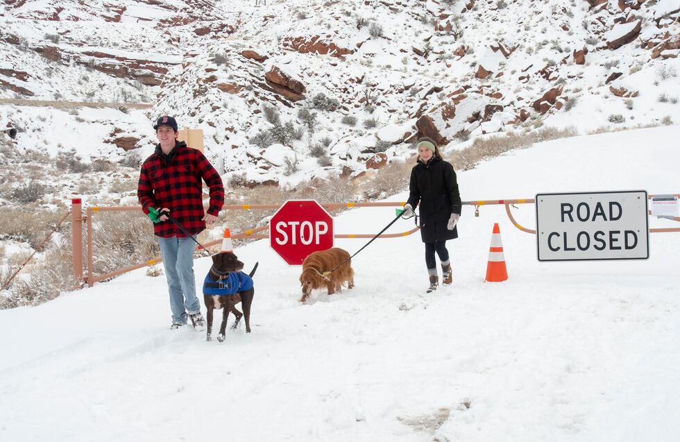 FILE - Parker Smith and Hillary Smith hike along a closed road outside Arches National Park in...